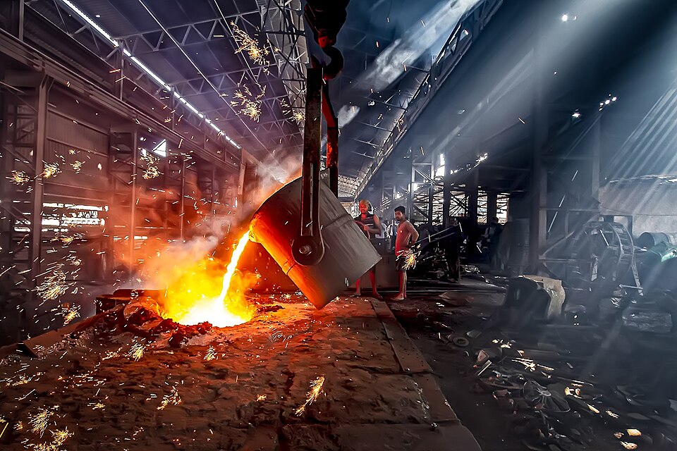 Metallurgical furnace in operation inside an industrial foundry in Guwahati, Assam, India, showing molten metal being poured and workers engaged in the smelting process.